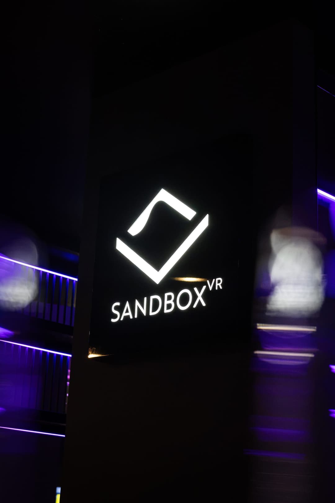 The illuminated Sandbox VR logo on a dark wall