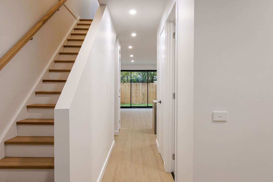 Hallway of a new townhouse, timber stairs and light floors through to the courtyard