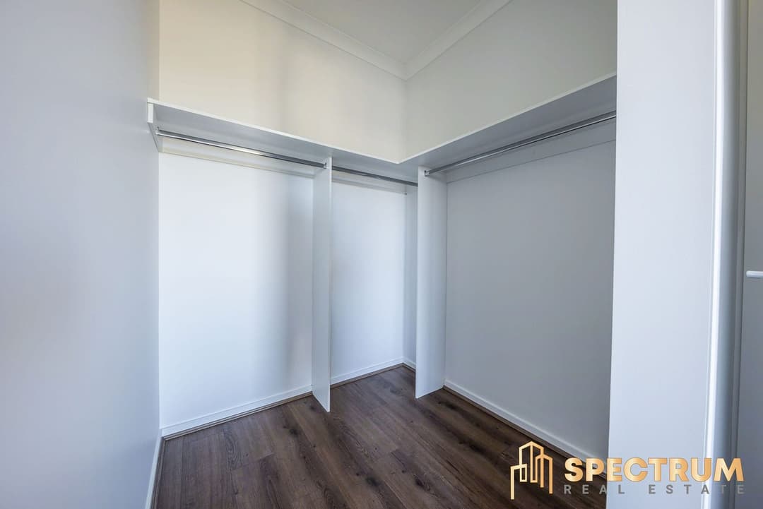 An empty walk-in robe with hanging rails and dark timber-look flooring. Frame 3 of 6. Open it