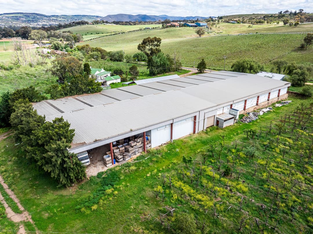 Drone view of a long packing shed on an orchard property, hills behind. Frame 2 of 6. Open it