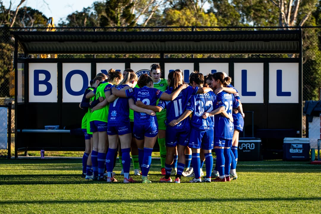 The Box Hill United women's team in a huddle in front of the dugout