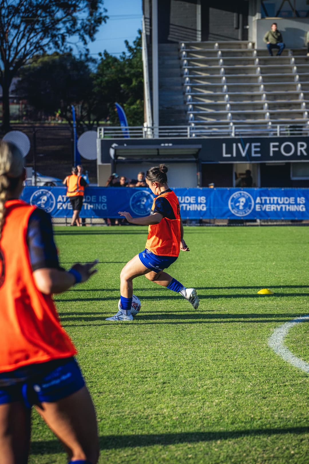 Box Hill United players in training bibs warming up in front of the ground boards