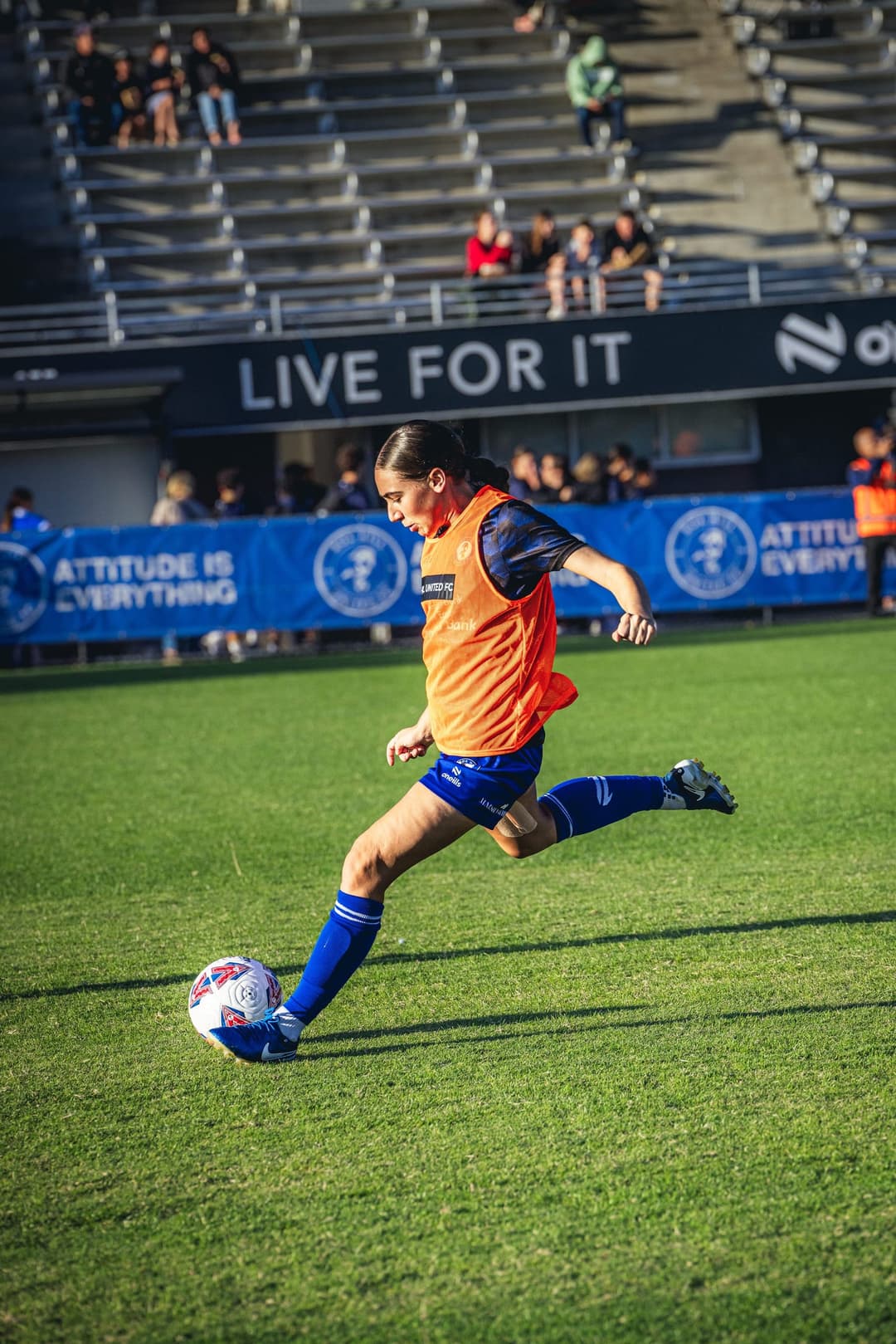 A Box Hill United player striking the ball in the warm-up, grandstand behind