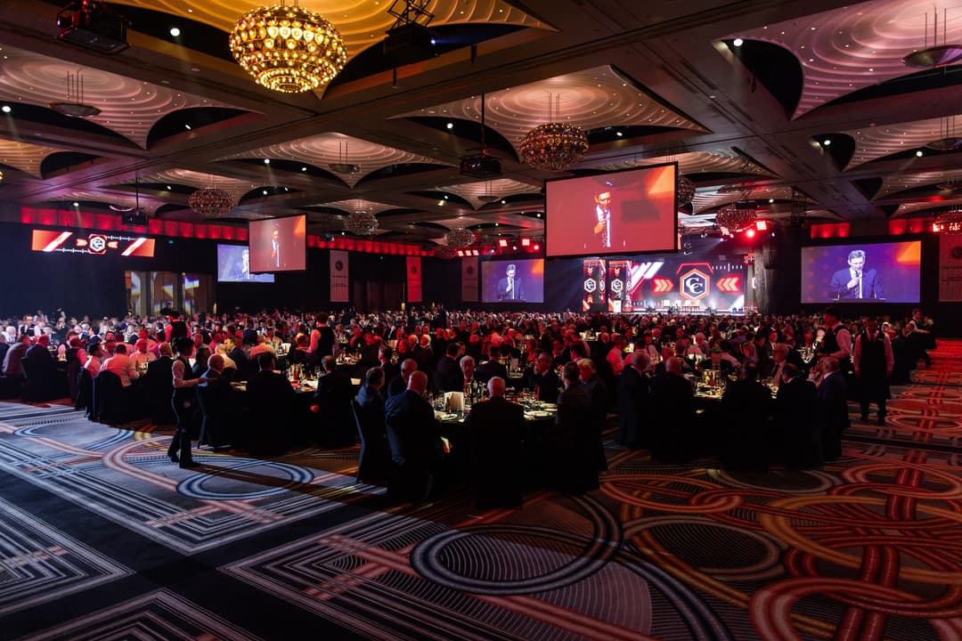 A packed ballroom of round tables under chandeliers, screens along the walls, Carbine Club lunch
