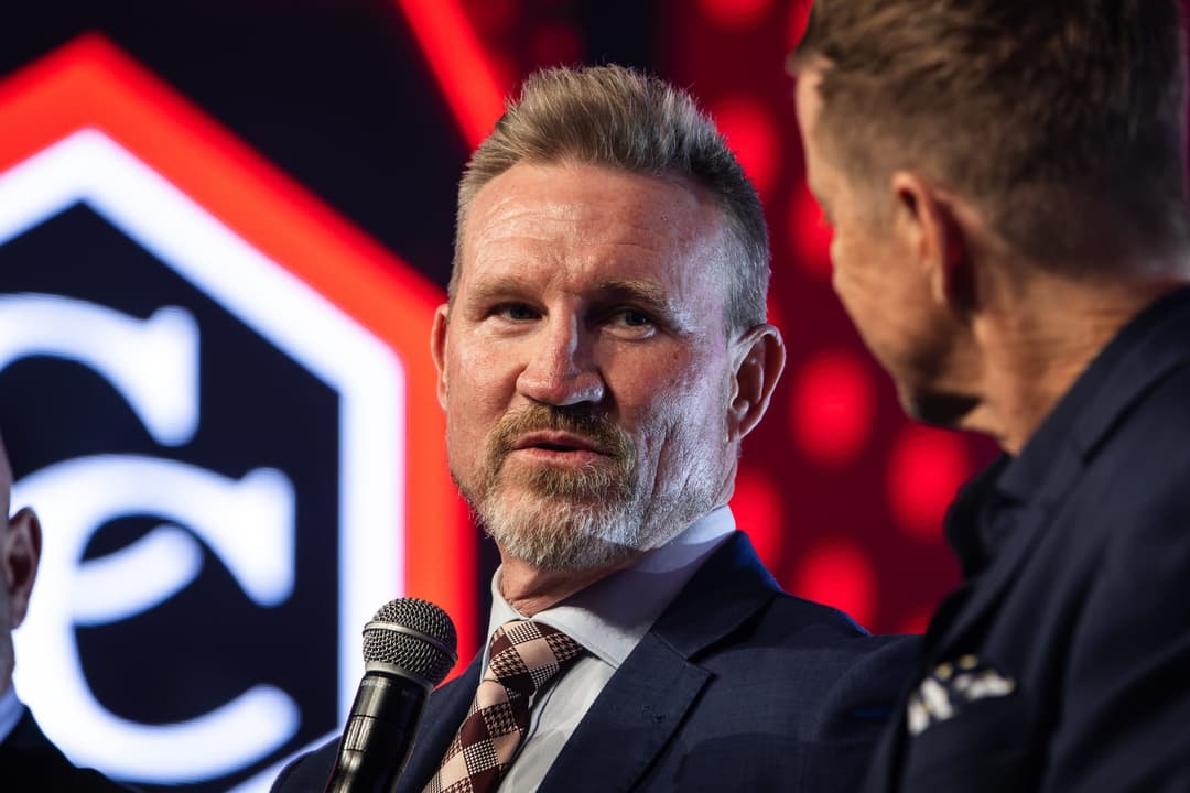 A panellist listening on stage, the Carbine Club mark behind him