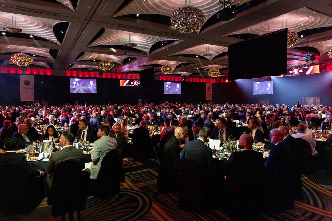 Guests at round tables across the ballroom, screens above