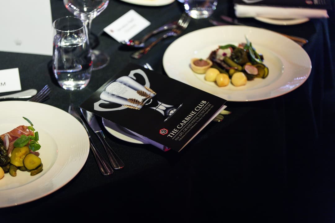 Plated entrées on a set table with a Carbine Club programme