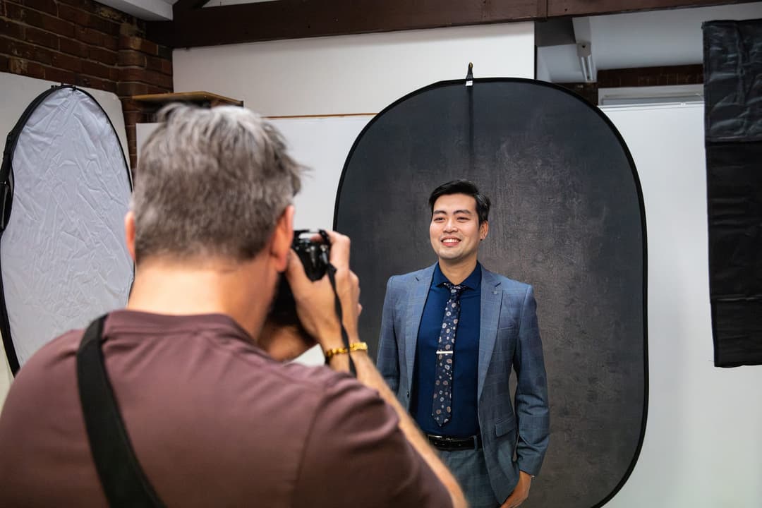 The photographer shoots a client in a blue suit on a dark backdrop.