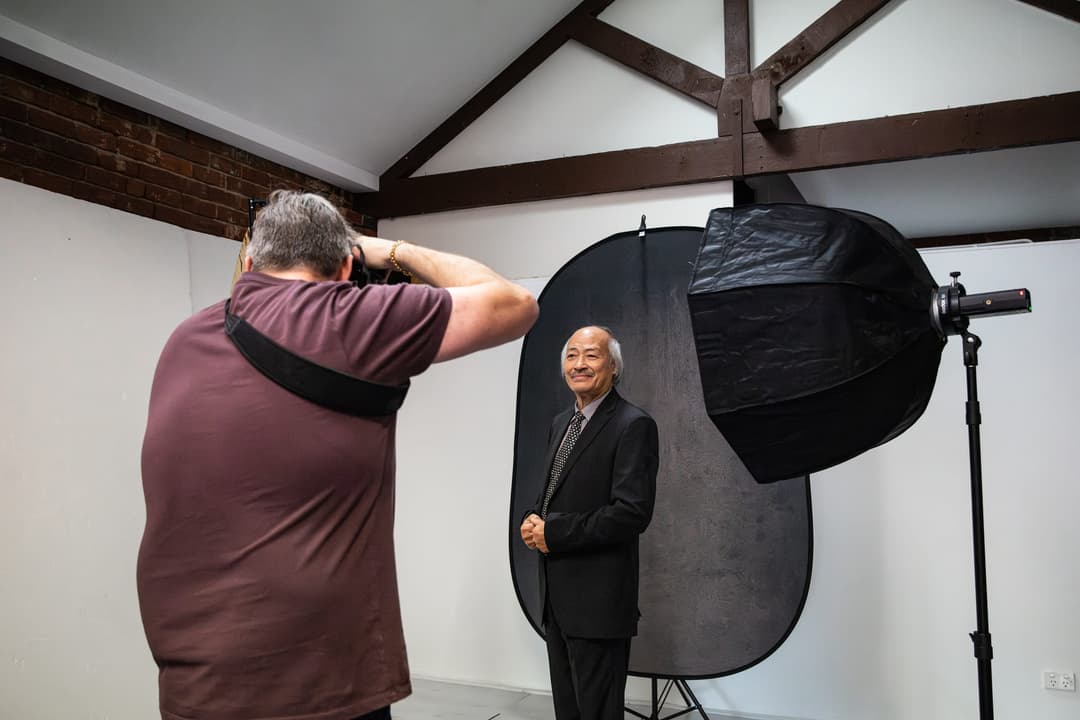 The photographer shoots a client on a dark backdrop under a softbox.