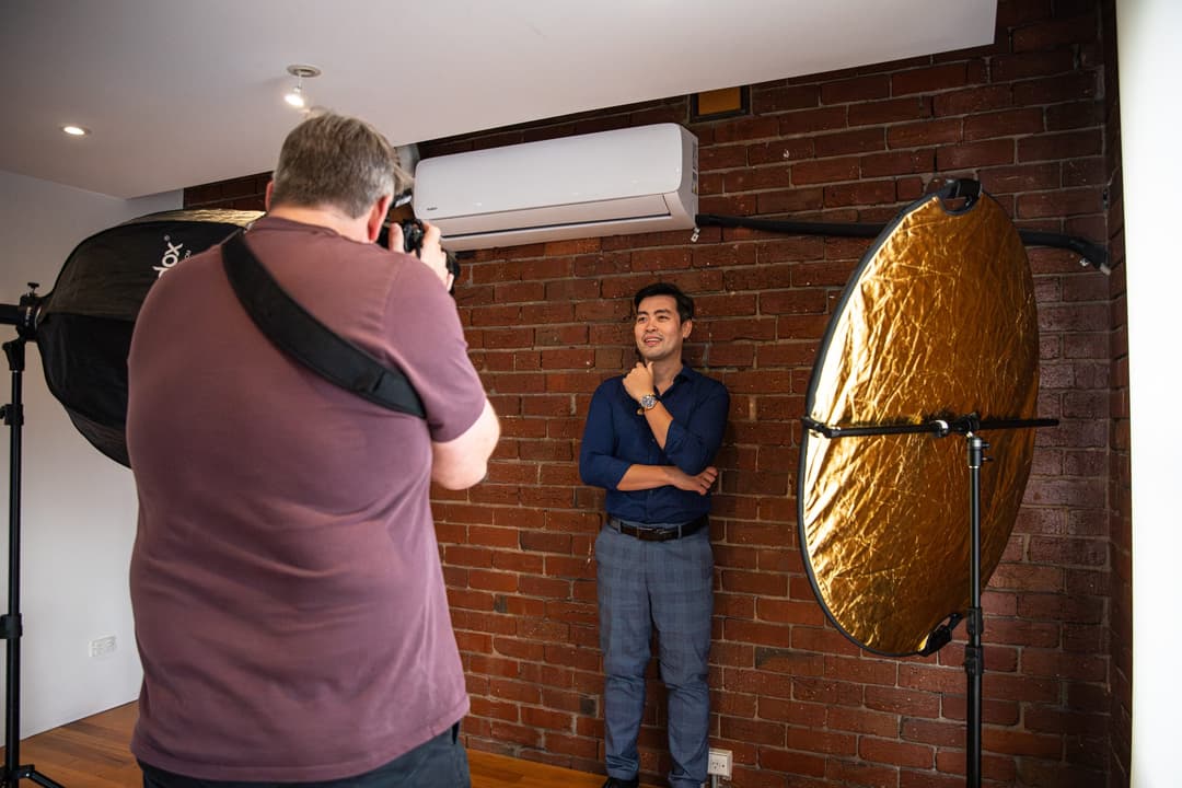 The photographer shoots a client in a navy suit beside a gold reflector.