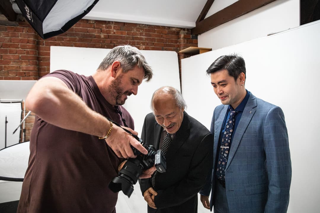 The photographer shows two clients in suits a frame on the camera.