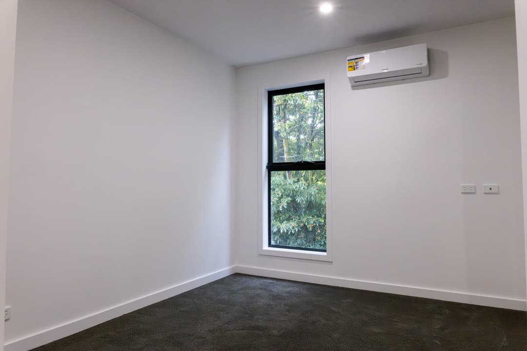 Empty bedroom with a black-framed window and a split-system unit